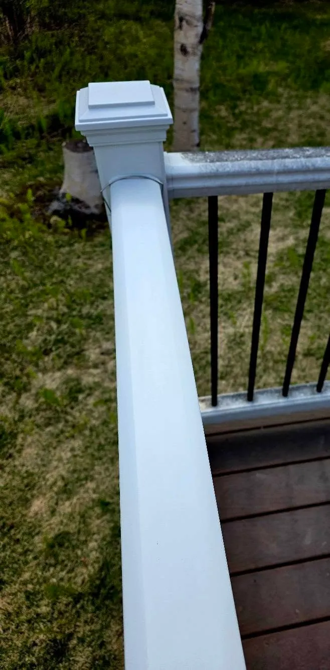 A white deck railing brightened, Alaska lawn behind it
