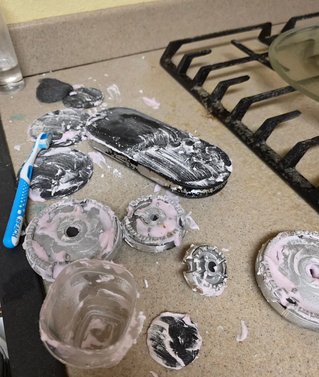 Stove burner caps being detailed by hand with a brush